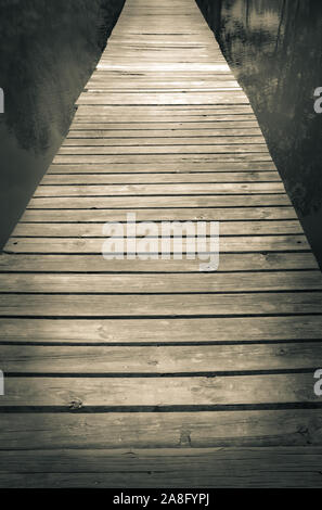 A mystical seeming wooden footbridge crosses the water at twilight with trees reflecting in water for a zen experience Stock Photo