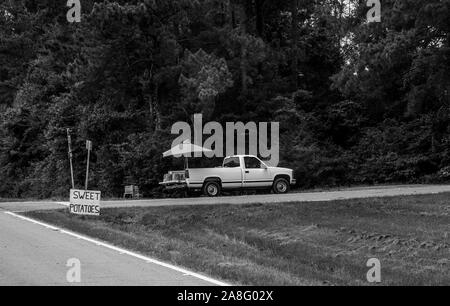 A produce vendor in a pickup truck on the side of the road with a sign for sweet potatoes in rural Southern Mississippi, USA, in black and white Stock Photo