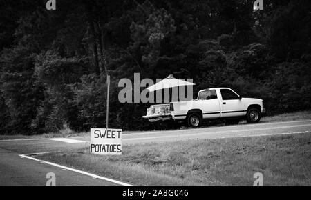 A produce vendor in a pickup truck on the side of the road with a sign for sweet potatoes in rural Southern Mississippi, USA, in black and white Stock Photo