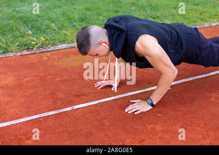 Young man doing push ups in the morning outdoor on the running race track Stock Photo