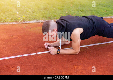 Young man doing plank exercise in the morning outdoor on the running race track Stock Photo