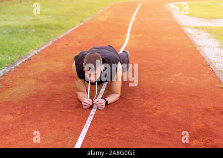Young man doing plank exercise in the morning outdoor on the running race track Stock Photo