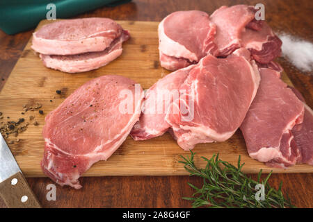 Raw Boneless Pork Loin chops on wooden cutting board with some herbs, salt, and rosemary close up on a wooden rustic background Stock Photo