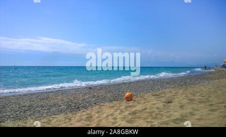 Orange ball at the sand beach near clean blue sea and clear blue sky. South Italy Stock Photo