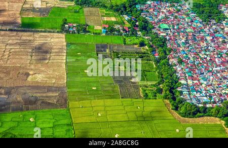 Aerial view showing expansion of urbanization and mass housing into agricultural land and rice fields in southeast Asia. Luzon island, Philippines. Stock Photo