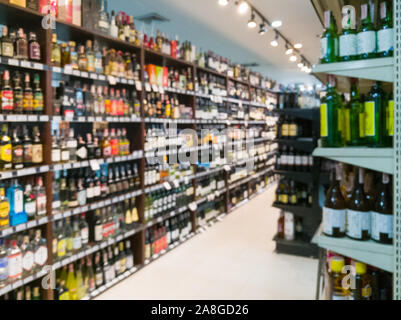Blurred image of wine shelves display in supermarket. Defocused Rows of Wine Liquor bottles on the store shelf. Alcoholic beverage abstract background Stock Photo