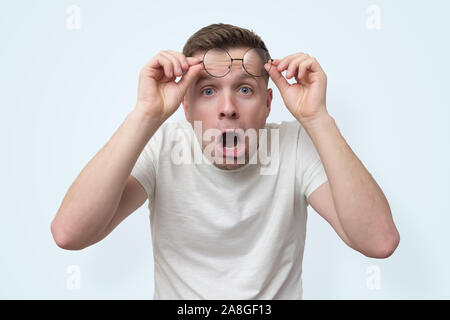 Surprised handsome man in glasses seeing something interesting. He is surprised with new prices on lens. Studio shot Stock Photo