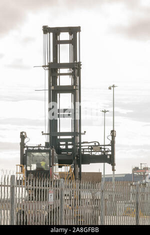 empty shipping container handler or forklift truck for use with heavy industrial loads,behind a steel fence at a factory site with male driver at work Stock Photo