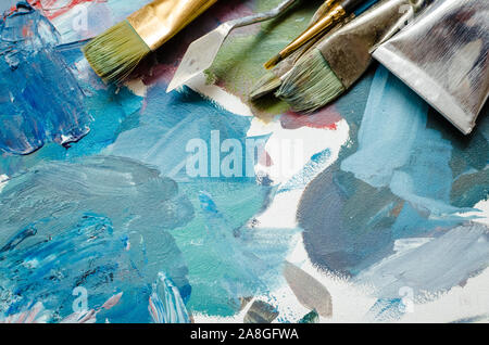 Artist paint brushes and oil paint tubes on wooden palette. Texture mixed oil paints in different colors. Instruments and tools for creative leisure. Stock Photo