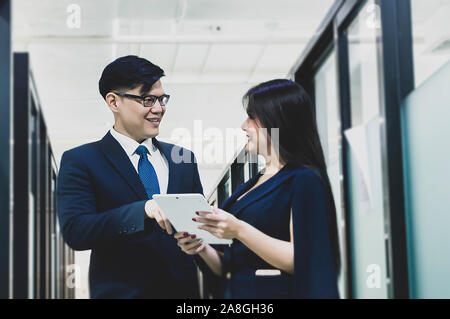 Asian business executive man and secretary standing in office hallway discussing tablet. Stock Photo