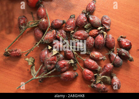 Pile of dried red fruits of the dog rose on the light-colored wooden rustic table . Hawthorn on wooden rustic table background. Rose hips haw fruit of Stock Photo