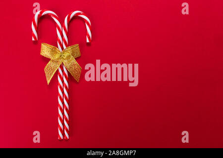 Two christmas candy canes with golden bow on red background. Copy space. Stock Photo