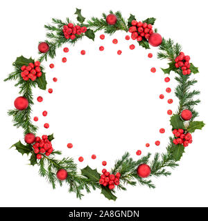 Winter and Christmas juniper fir wreath with red baubles & loose red holly berries on white background with copy space. Traditional xmas symbol. Stock Photo