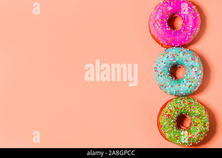 Closeup of three multicolored pink, blue and green glazed sweet donuts on coral background with copy space Stock Photo
