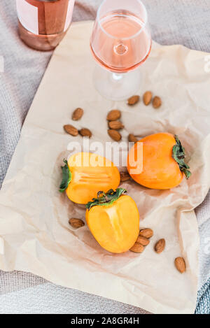 Picnic on the beach with persimmons, almond and bottle of rose wine on beige blanket. Stock Photo