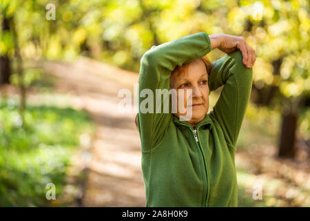 Senior woman is exercising in park on sunny day. Stock Photo