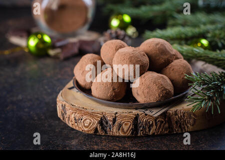 Homemade chocolate truffles on the paper on stone concrete table background with festive holiday decoration. Christmas Dessert Stock Photo