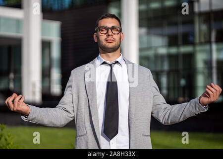 Young businessman is meditating outside the company building. Stock Photo
