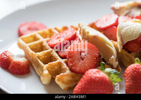 Strawberry waffles. Selective focus closeup of red fruit on authentic homemade sweet pancake waffle. Serving with icecream served on a white plate bac Stock Photo