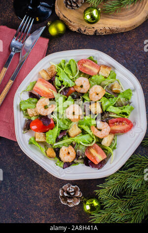Fresh caesar salad with shrimps on white plate dark stone table background with Christmas Festive Decoration. Healhty Food Snack Concept. Top view Cop Stock Photo