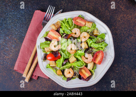 Fresh caesar salad with shrimps on white plate dark stone table background. Healhty Food Snack Concept. Top view Copy Space Stock Photo