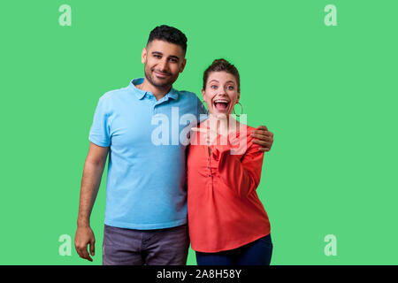 That's him! Portrait of happy young couple in casual wear standing and hugging as friends, woman pointing finger at man, looking shocked at camera. is Stock Photo