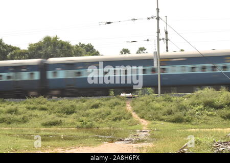 express train moving on the railway track, blur view with green grass and green plants in india. Stock Photo