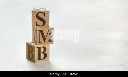 Pile with three wooden cubes - letters SMB meaning Small to medium sized business on them, space for more text / images at right side. Stock Photo