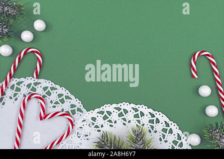 Seasonal Christmas flat lay with white lace doily, traditional candy canes and fir branches with snow balls on green copy space Stock Photo