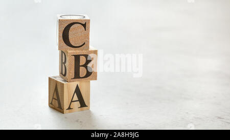 Pile with three wooden cubes - letters CBA meaning Cost Benefit Assessment on them, space for more text / images at right side. Stock Photo
