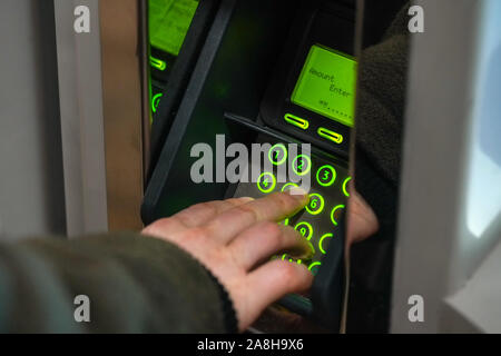 Man about to withdraw money from ATM / top up travelcard, detail to fingers entering amount on green terminal. Stock Photo