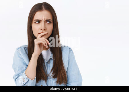 Pensive, serious-looking focused caucasian woman in denim jacket, touching lip thoughtful, frowning intense and looking sideways as thinking, having Stock Photo