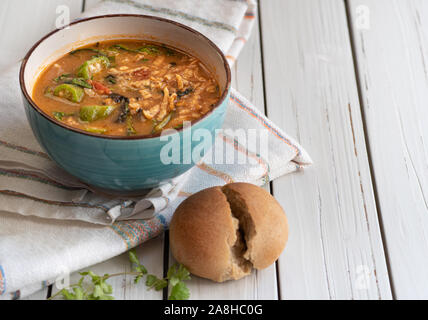 Hearty vegan soup with brown rice, okra and spinach, served in a bowl on a white wooden table Stock Photo