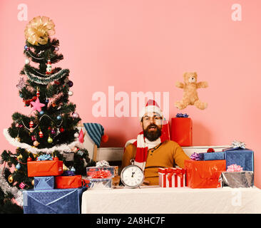 Christmas tree with Santa throwing teddy bear up and sits near gift boxes on pink background. Christmas eve and New Year concept Stock Photo