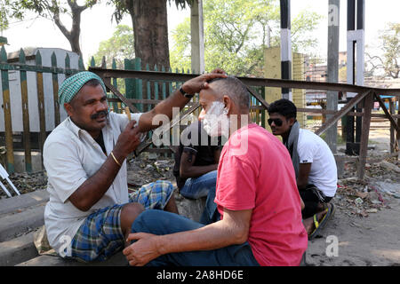 Street barber shaving a man using an open razor blade on a street in Kolkata, West Bengal, India Stock Photo