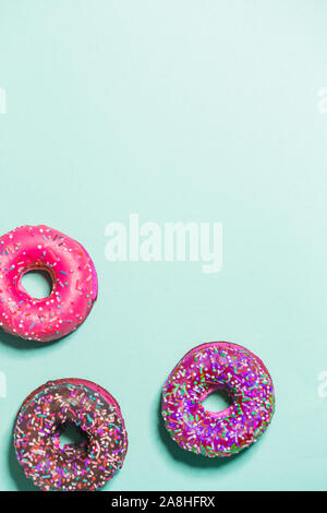 Closeup of three multicolored glazed sweet donuts on a blue background, top view, copy space. Food, restaurant, bakery concept Stock Photo