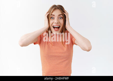 Waist-up surprised, amused pretty girl in striped t-shirt, smiling joyfully from amazement, feeling excited hearing awesome news, touch head and stare Stock Photo