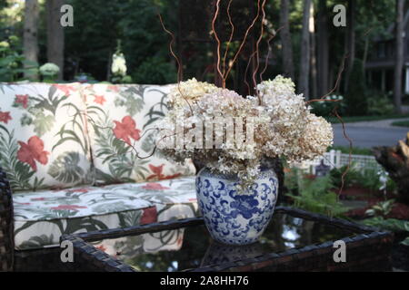 Outdoor seating arrangement  with wicker, and a table with dried hydrangea  in a vase Stock Photo
