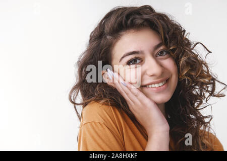 Tender delighted young flirty caucasian girl curly black hair pressing palm cheek blushing nice heartwarming compliment smiling broadly feel upbeat in Stock Photo