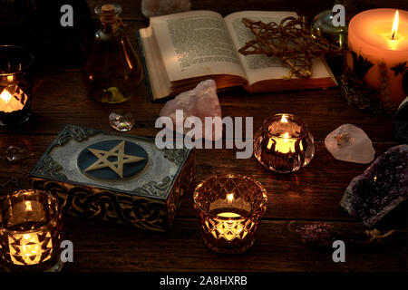 Esoteric or mystical still life with a box and a few burning candles, a pentagram next to an open book. Pendulum and precious stones on old wooden tab Stock Photo