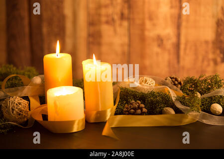 The warmth of the Christmas concept: three candles lit on a dark wooden table and a rustic wooden setting with pine branches, natural pine cones and g Stock Photo