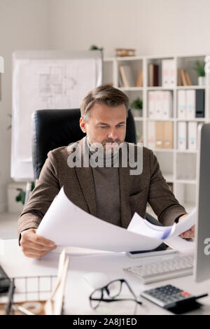 Serious mature architect in formalwear looking through papers or blueprints Stock Photo