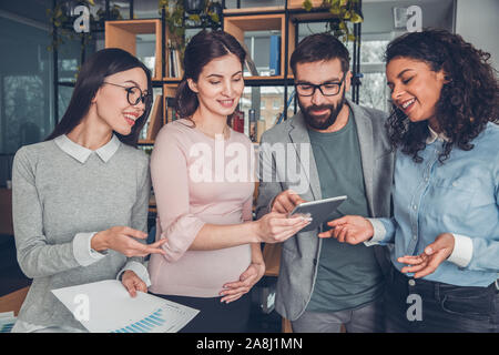 Startupers working together at office standing browsing internet on digital tablet joyful Stock Photo