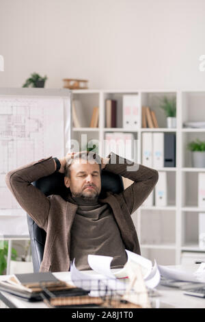 Mature engineer in formalwear sitting in armchair with his hands behind head Stock Photo