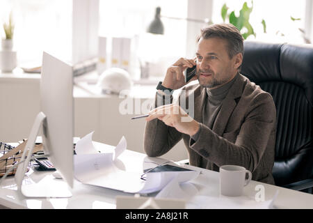 Confident architect talking on the phone while pointing at computer screen Stock Photo