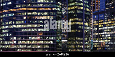 Glass walls of modern office buildings with many large panoramic windows in downtown business cluster with working people panoramic front view at nigh Stock Photo