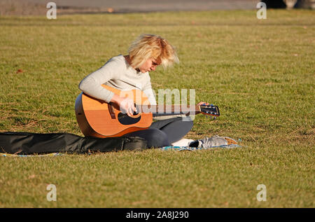 A young woman tunes her guitar while sitting in a public park along the Deschutes River in Bend, Oregon Stock Photo