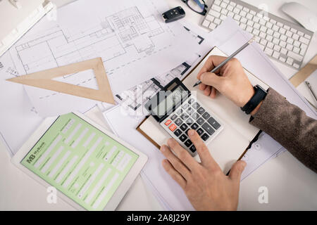 View of hands of engineer with pen and calculator making notes in notebook Stock Photo