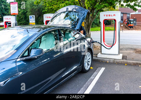 A man charges his car at the Tesla charging station at the motorway services in the UK, electric charging Stock Photo
