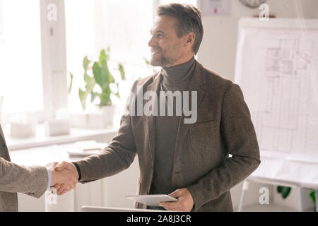 Happy successful engineer with touchpad shaking hand of new business partner Stock Photo